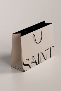 a white shopping bag with the word saint printed on it, sitting in front of a grey background