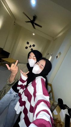 two people wearing face masks standing next to each other in front of a ceiling fan