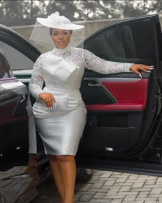 a woman in a white dress and hat standing next to the door of a car