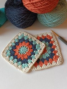 two crocheted coasters sitting on top of a table next to balls of yarn