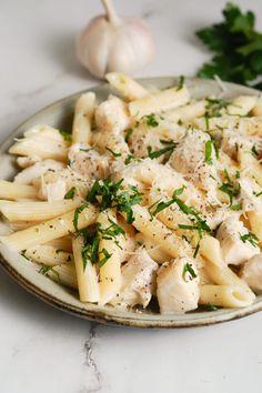 a plate full of pasta with chicken and parsley on it next to some garlic