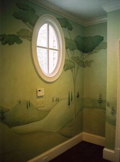 an empty room with a round window and painted trees on the wall in front of it