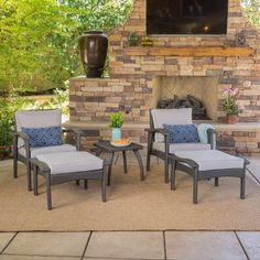 a patio with chairs, tables and a television mounted on the brick wall above an outdoor fireplace