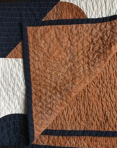 an orange and blue quilt on top of a white bed sheet with black trimmings