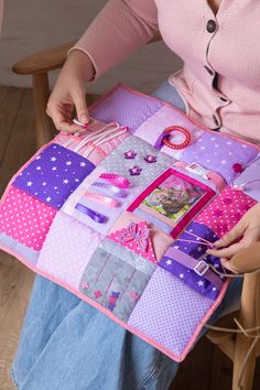 a woman sitting in a chair holding a patchwork quilt with pictures and pins on it