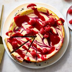 a cheesecake with raspberries and cream on a plate next to a knife