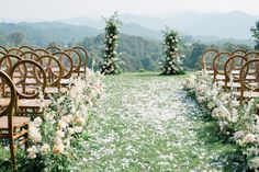 an outdoor ceremony set up with wooden chairs and flowers on the aisle, surrounded by greenery