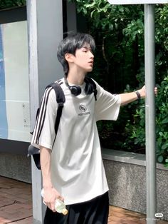 a young man standing next to a street sign with headphones on and holding something in his hand