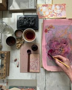 a person is painting on a piece of paper with watercolors and paintbrushes