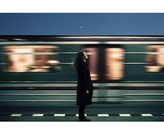 a woman standing in front of a train at night with motion blurs behind her