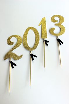 three gold and black cake toppers with the numbers 2013 on them, sitting in front of each other