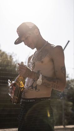 a shirtless man with tattoos holding a bottle