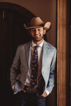 a man in a suit and tie standing next to a wooden door wearing a cowboy hat