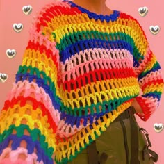 a woman wearing a multicolored knitted sweater and green pants with hearts on the wall behind her