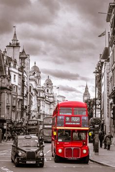 a red double decker bus driving down a street next to tall buildings and people walking on the sidewalk