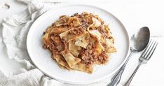 a white plate topped with pasta and meat next to two silverware on top of a table