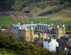 a large building with many windows and towers in the middle of a green field next to mountains