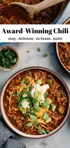 a bowl of chili with cheese and avocado in it, next to another bowl full of chili