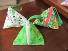 three small triangle shaped purses sitting on top of a wooden table