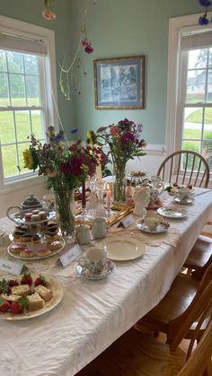 the table is set with tea cups, plates and flowers in vases on it