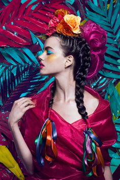 a woman with braids and flowers in her hair wearing a red dress surrounded by tropical leaves