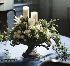 a centerpiece with white flowers and candles on a table in front of a window