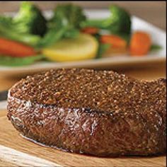 a piece of steak sitting on top of a wooden cutting board next to a plate of vegetables