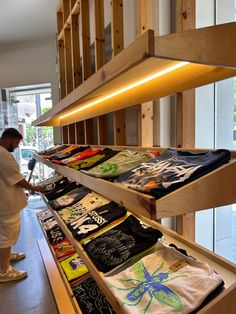 a man is looking at t - shirts on display in a store with wooden shelves