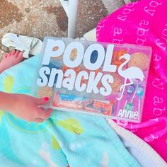 a baby laying on top of a towel next to a pool snack box with snacks in it