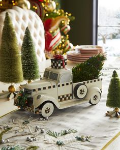 a toy truck with christmas trees in the back is on a table next to other decorations