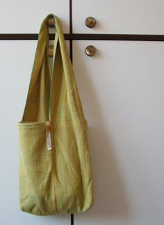 a green bag hanging on the wall next to a hook with two buttons and a tag