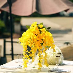 yellow flowers are in vases on a white table with silverware and wine glasses