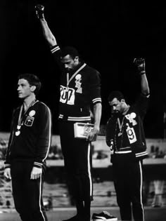 three men standing on top of a track holding their hands up in the air while one man stands next to them