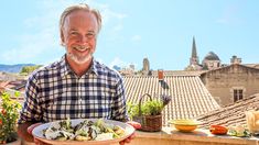 a man holding a plate of food on top of a roof with buildings in the background