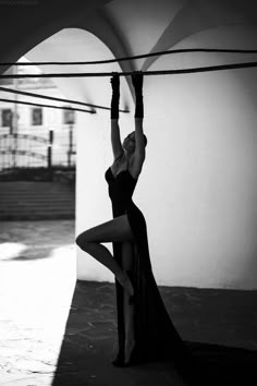 a woman in a long black dress is hanging upside down on a rope with her hands