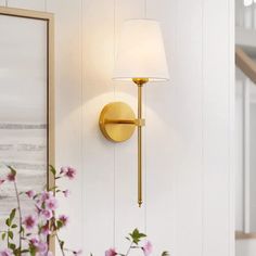 a lamp that is on the side of a wall next to flowers and a vase