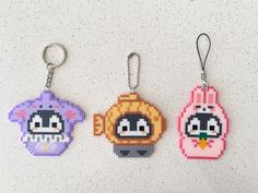 three keychains made to look like cartoon characters are hanging on a white surface