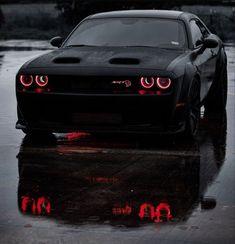 a black sports car with red lights on it's headlight is parked in the rain