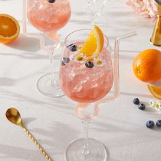 three glasses filled with pink lemonade, blueberries and orange slices on a table