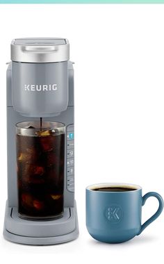 a keurig coffee maker next to a cup of tea and a blue mug