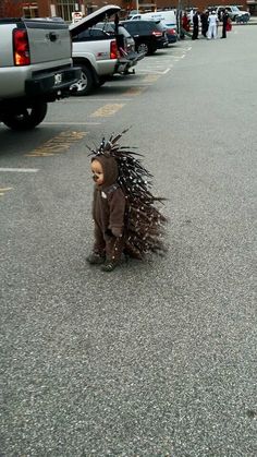 a small child in a costume is walking down the street with feathers on his head