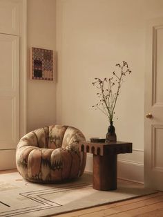 a living room with a chair, table and vase on the floor in front of it