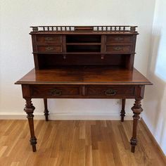 an old wooden desk sitting on top of a hard wood floor next to a white wall