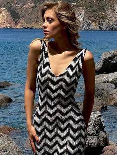 a woman standing on rocks near the water wearing a black and white chevron dress