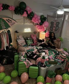 a room filled with lots of green and pink balloons hanging from the ceiling next to a bed