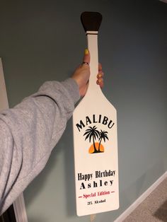 a person holding up a bottle shaped like a paddle with the name malibu on it