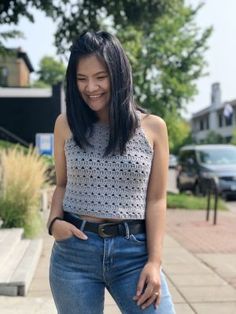 a woman standing on the sidewalk with her hands in her pockets and smiling at the camera