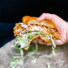 a hand holding a sandwich with lettuce and cheese on it, in front of a black background