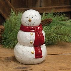 a snowman statue sitting on top of a wooden table next to pine cones and needles