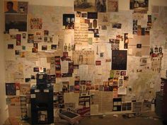 a wall covered in papers and pictures next to a trash can with a tv on it